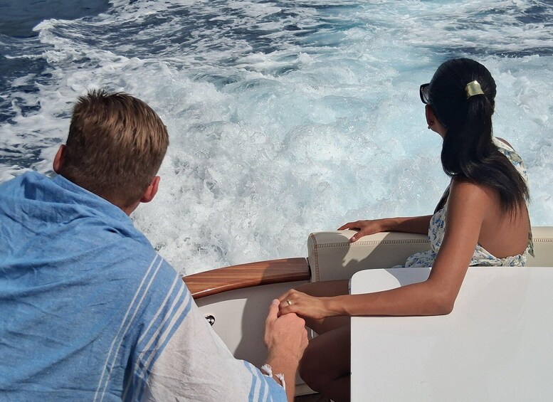A man and a woman sitting on a boat, looking at the ocean waves. 2