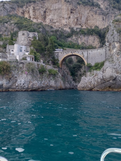 A stone bridge over a body of water, with buildings and cliffs in the background. 5