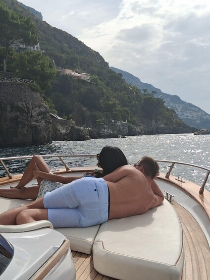 Two people relaxing on a boat with a mountainous coastline in the background. 3