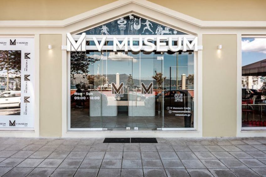 The MV Museum entrance with a clear glass facade, a tiled pavement, and a mountain in the background. 2
