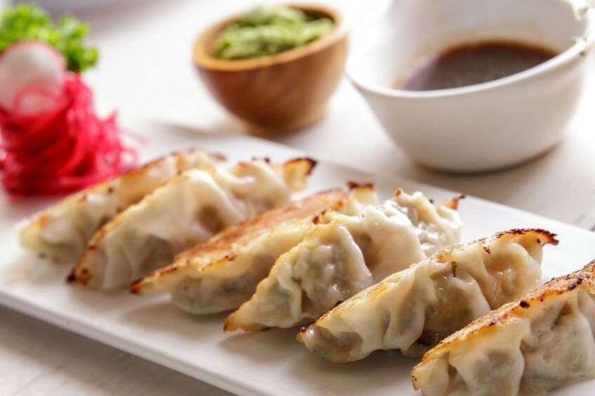 A plate of golden-brown dumplings with a side of dipping sauce and pickled vegetables. 5