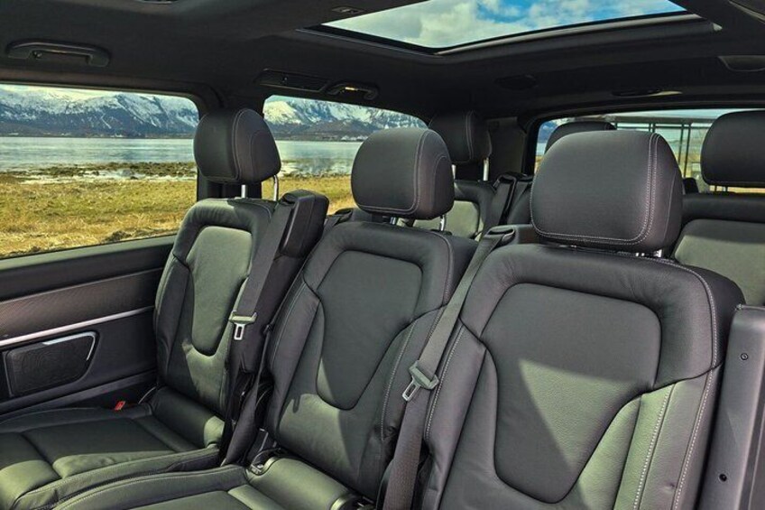 A car interior with black leather seats, a sunroof, and a view of a lake and mountains. 2