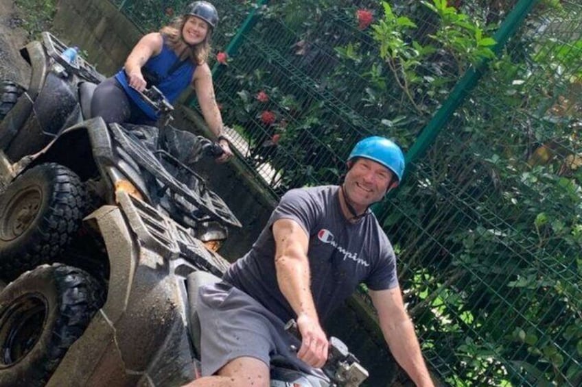 Two people on all-terrain vehicles in a fenced area with greenery. 5
