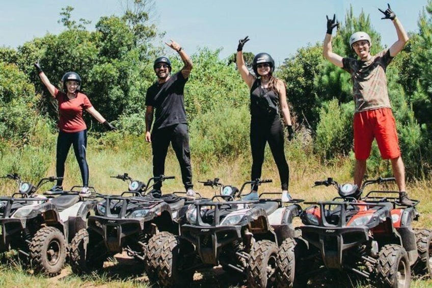 Four people standing on ATVs with a forested landscape in the background. 1