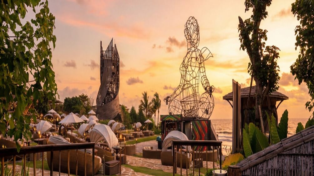 Et strandresort i solnedgang med udendørs siddepladser, en unik skulptur og en pavillon. 4