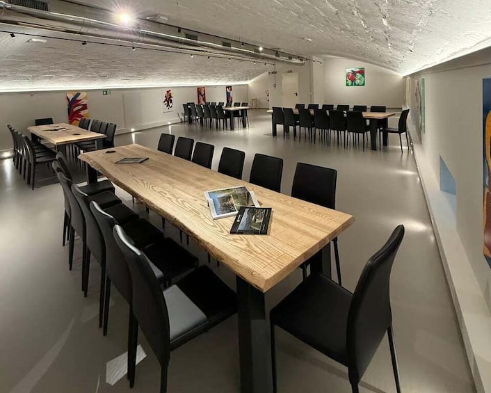 A conference room with a long wooden table, black chairs, and a white ceiling with exposed pipes. 3