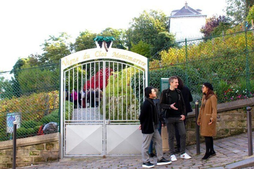Un cancello in metallo con la scritta 'Vigne au Clos Montmartre', circondato da vegetazione e un muro di pietra. 3