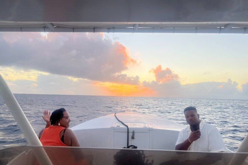 A boat with two people, one wearing an orange top and the other in white, with a sunset over the ocean. 3