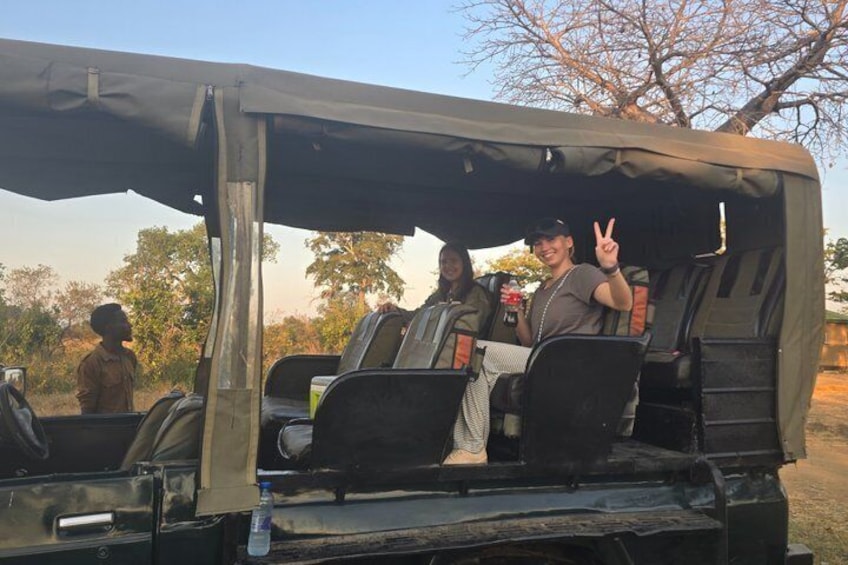 Un véhicule de safari avec une partie arrière ouverte, une personne faisant le signe de la paix, et un arbre en arrière-plan. 5