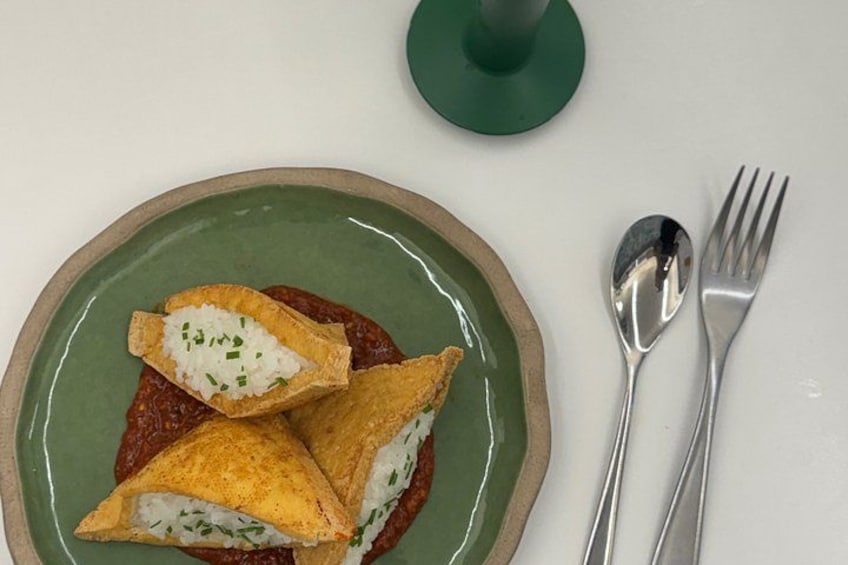 Une assiette contenant trois aliments de forme triangulaire, une cuillère et une fourchette, posée sur une table blanche. 3