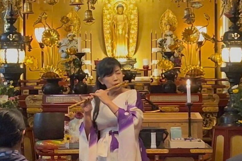 En person i traditionell dräkt utför en ritual i ett tempel, omgiven av statyer och rökelsekar. 3