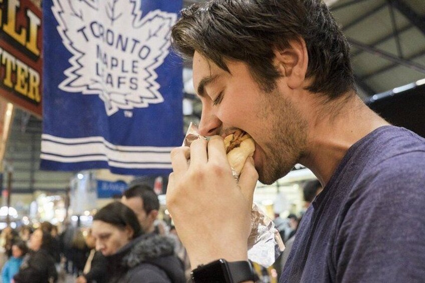 A person eating a hot dog at an outdoor event with a banner in the background. 2