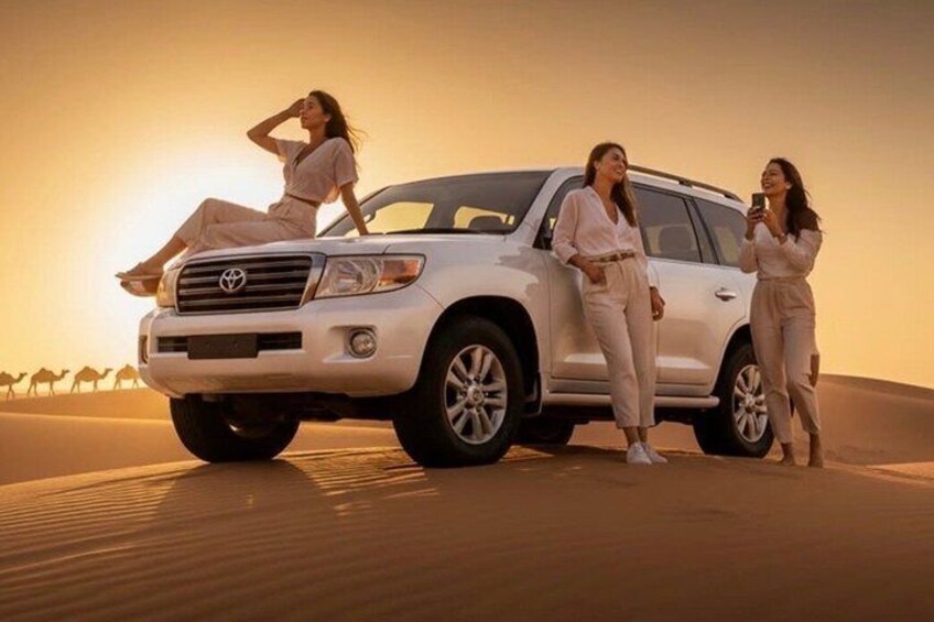 A white SUV parked on sand dunes with three people around it. 5