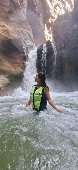 A person in a life jacket standing in a river with a waterfall in the background. 5