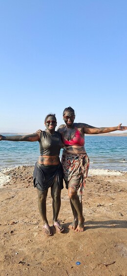 Two people standing on a beach with their arms outstretched, wearing mud-covered clothing. 2