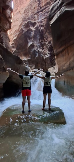 Two people standing on a rock with arms outstretched in a canyon with water flowing around them. 5