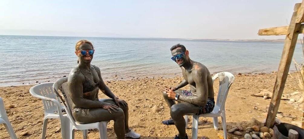 Two people sitting on plastic chairs on a sandy beach with a calm sea in the background. 3