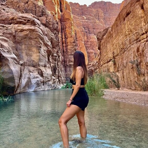 A person standing in a river with red rock cliffs in the background. 1