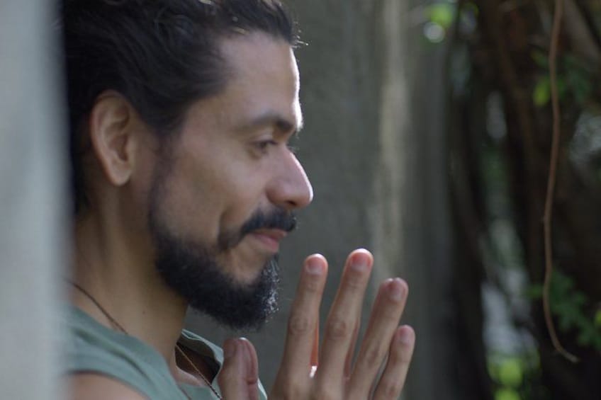 A person with a beard, wearing a sleeveless top, with their hand partially visible. 3