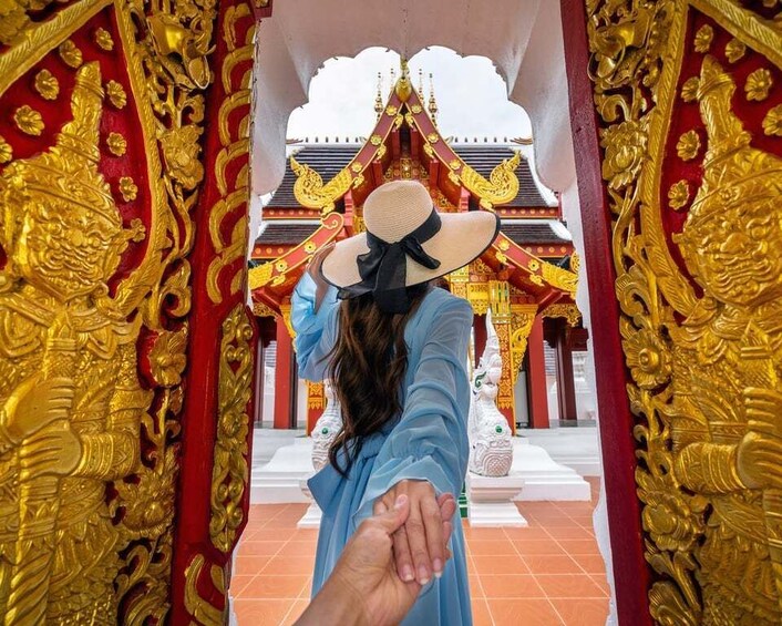 A person holding hands with another, facing a temple entrance with ornate golden decorations and a white structure in the background. 2
