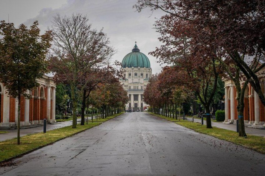 A wide, wet street lined with trees and buildings, leading to a large building with a green dome. 3