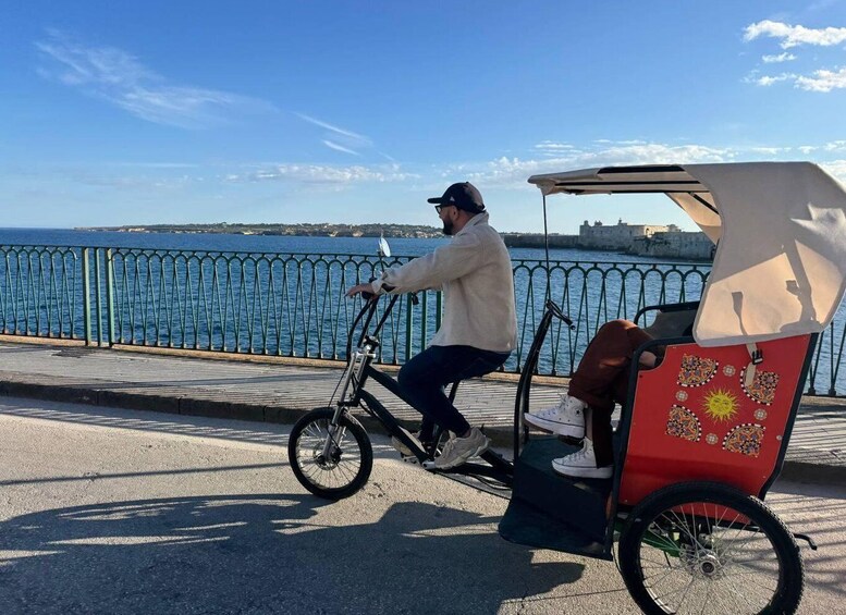 A person riding a bicycle with a cart attached, on a paved path by the sea. 5