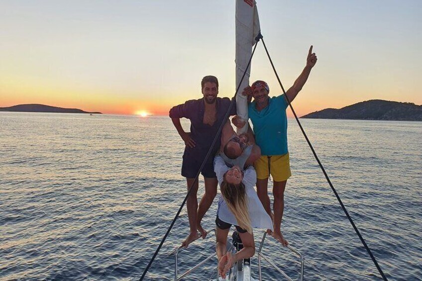 Eine Gruppe von Menschen auf einem Segelboot bei Sonnenuntergang, ruhiges Wasser und eine entfernte Küste. 2