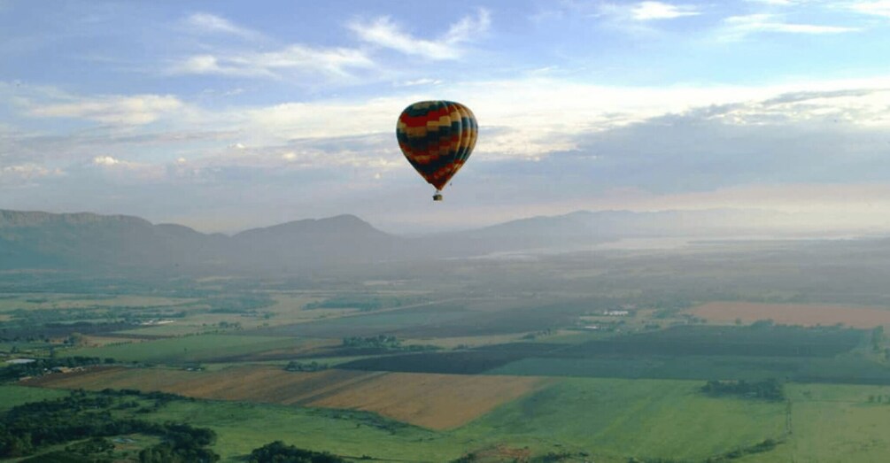 A hot air balloon over a rural landscape with fields and distant mountains. 4