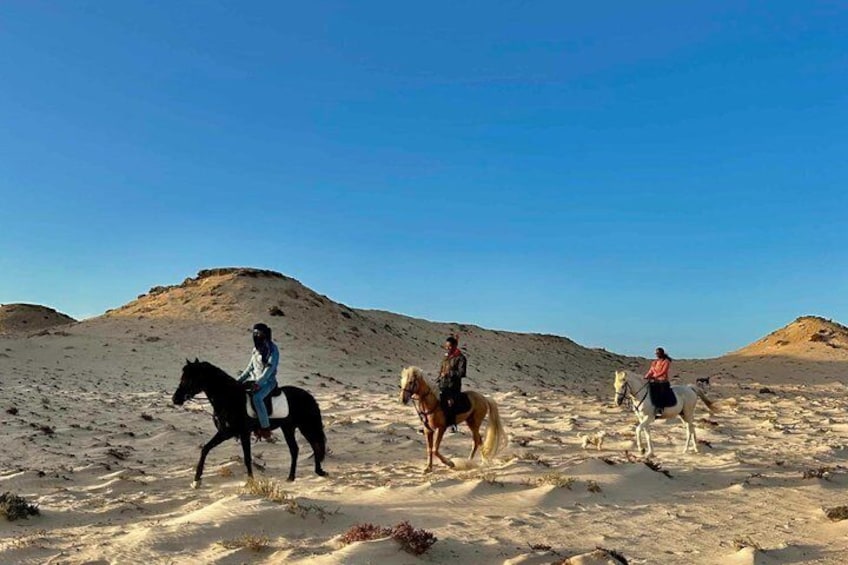 Three riders on horses in a desert landscape with sand dunes and clear skies. 4