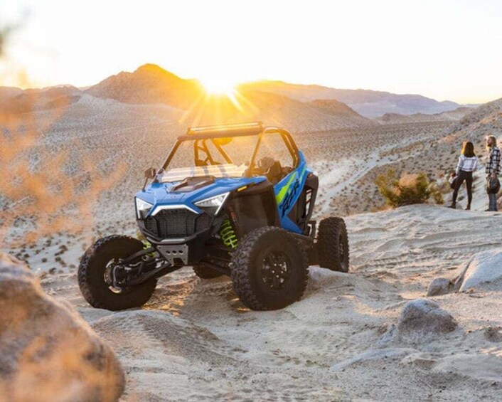 A blue off-road vehicle on a rocky terrain with a sunset in the background. 4