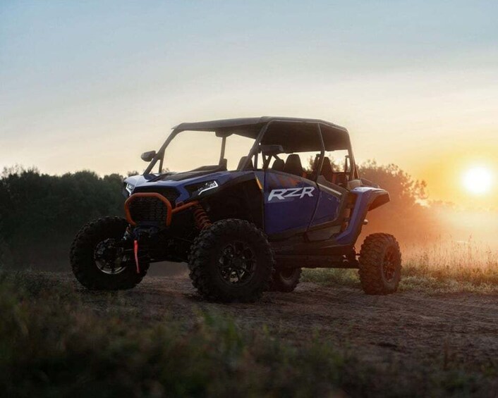 A RZR off-road vehicle on a dirt path with a sunset in the background. 1