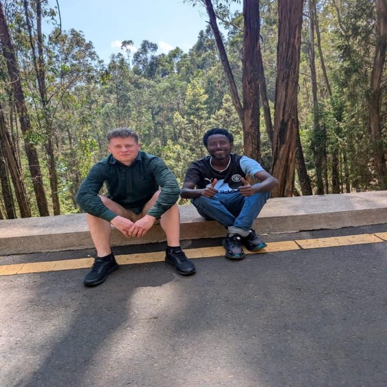 Two individuals sitting on a concrete ledge with a forested background. 1