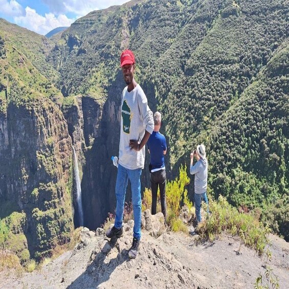 A person standing on a rocky outcrop with a waterfall in the background. 2