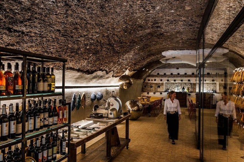 Un bar subterráneo con estantes de madera llenos de botellas, una barra y un techo rústico. 2