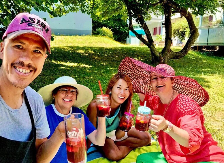 A group of people sitting on grass, holding drinks, with trees and a building in the background. 5