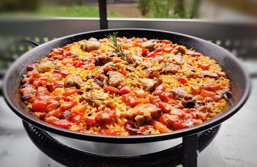 A large pan filled with a rice dish, possibly paella, with visible ingredients like chicken, red bell peppers, and herbs. 5