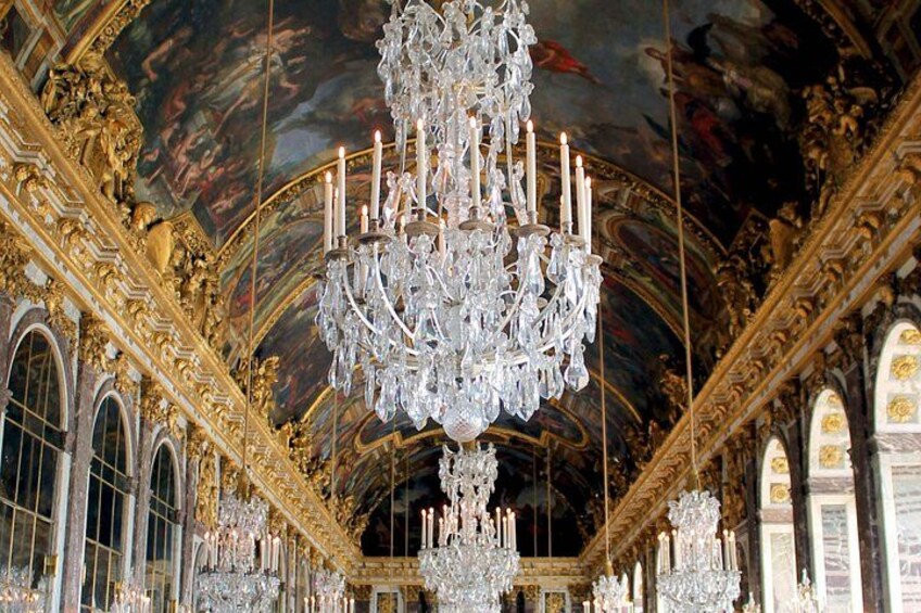 An ornate room with a large crystal chandelier, golden architectural details, and arched windows. 4