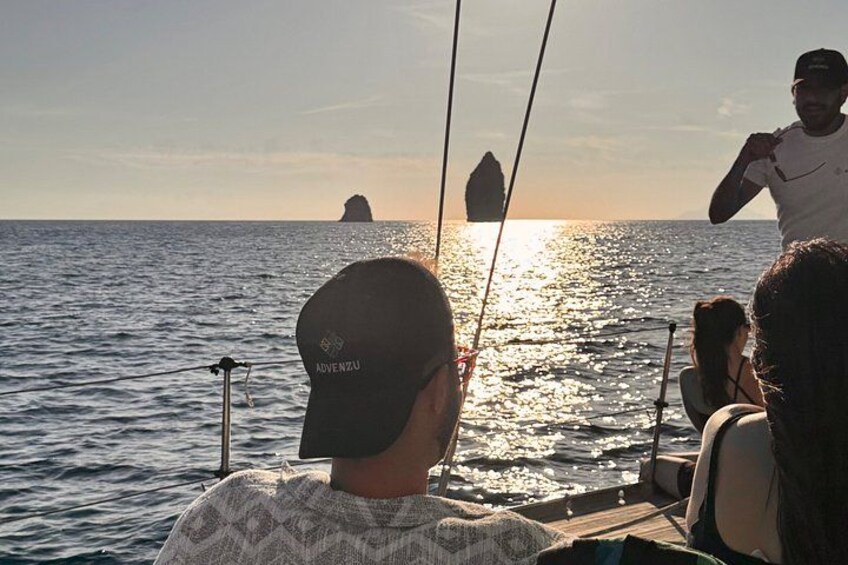 A boat with people on board, a person wearing a cap with 'ADVENTUZ' on it, and a distant island in the water. 2
