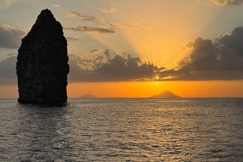 A rock formation in the ocean with a sunset in the background. 5