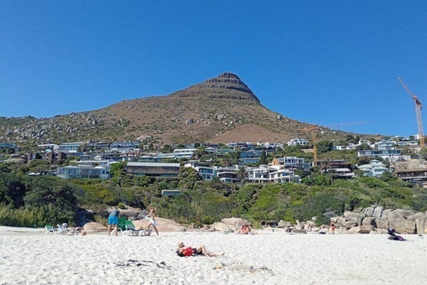 A beach with people sunbathing, a mountain in the background, and a construction crane. 1