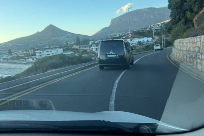 A car driving on a coastal road with a mountain in the background. 4