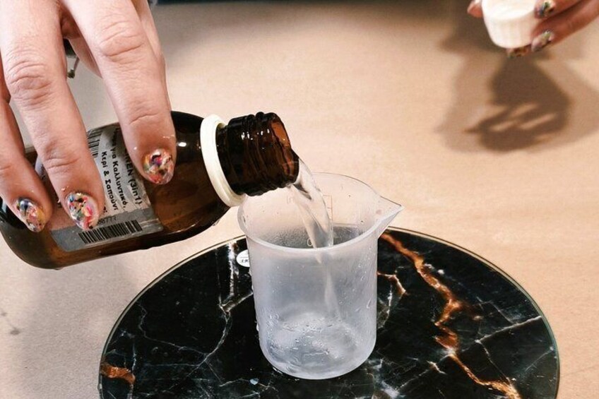 Una mano vertiendo líquido de una botella en una taza medidora transparente sobre una superficie de mármol. 5