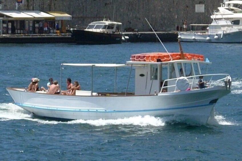 A white boat with blue stripes and an orange canopy, carrying passengers, moving through calm water. 1