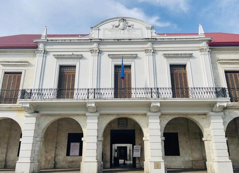 A historic building with a red roof, white facade, and a balcony with a blue flag. 5