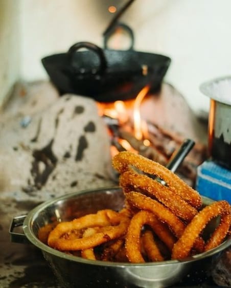 A metal bowl filled with fried onion rings, a black pot, and a blue container with a white lid. 3