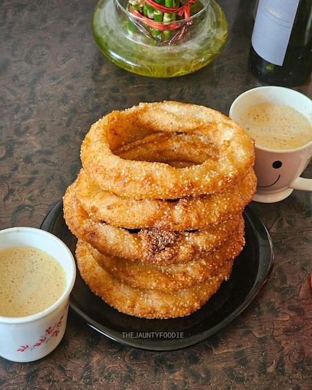 A stack of fried dough rings on a plate, accompanied by two cups of coffee. 1