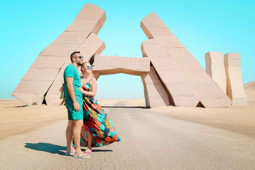 A couple standing in front of large, abstract stone structures in a desert landscape. 2