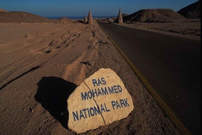 A road with a sign reading 'RAS MOHAMMED NATIONAL PARK' and a desert landscape with hills in the background. 3