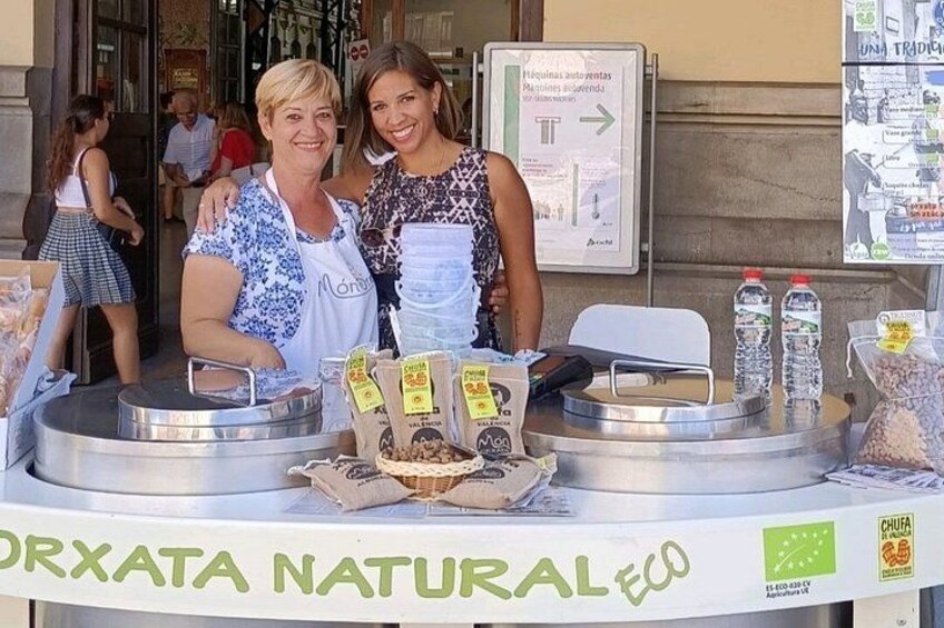 Ein Essensstand mit einem Schild, auf dem 'ORXATA NATURAL ECO' steht. Zwei Personen stehen hinter dem Stand, und es werden verschiedene Speisen präsentiert. 3