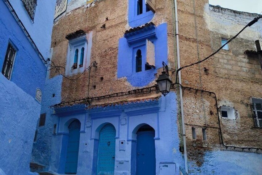 A narrow alley with buildings painted in blue and beige, featuring arched doorways and a street lamp. 5